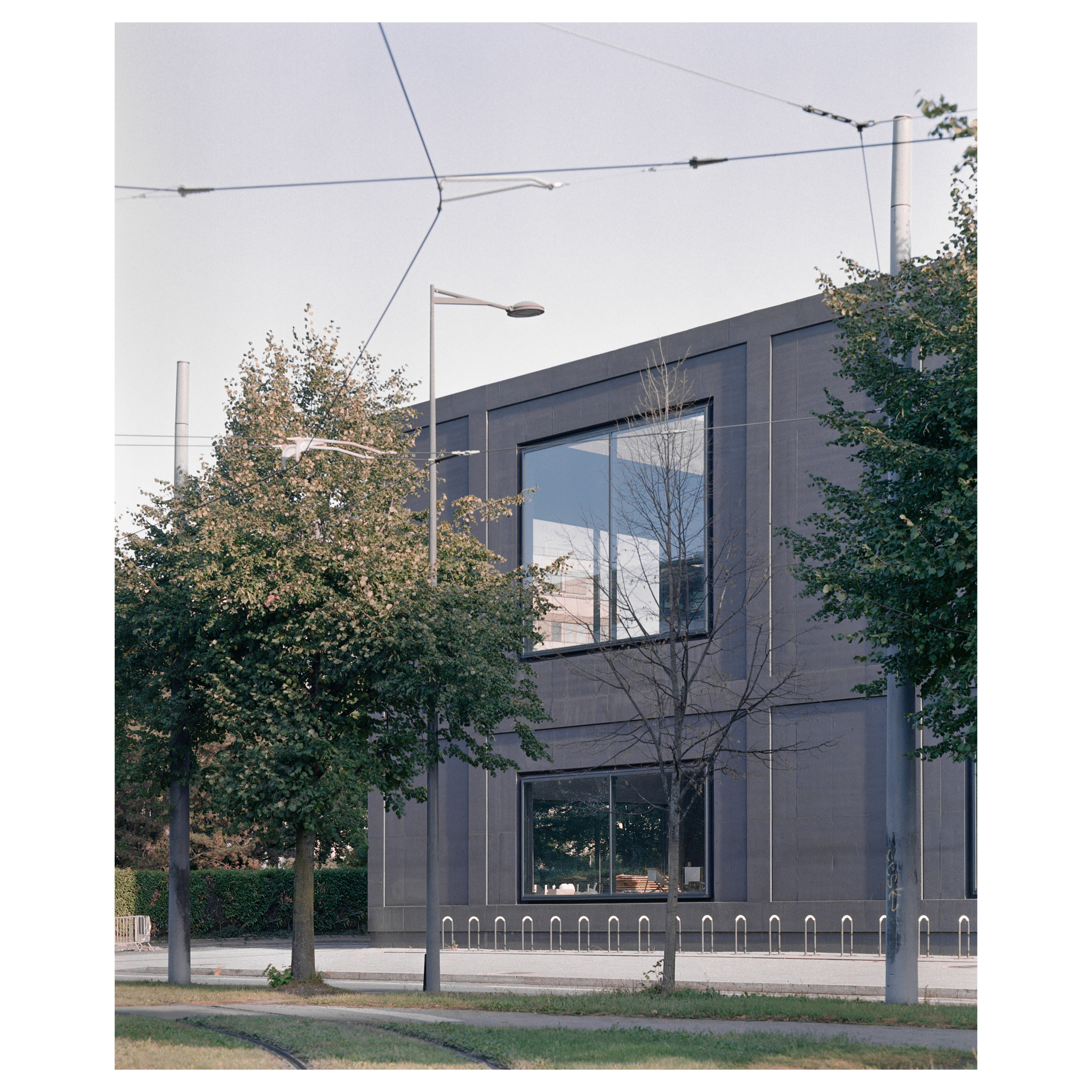 Photographie argentique du théâtre du maillon à Strasbourg (France) et construit par l'agence d'architecture parisienne LAN. Façade à travers le contexte végétal © Guillaume Porche